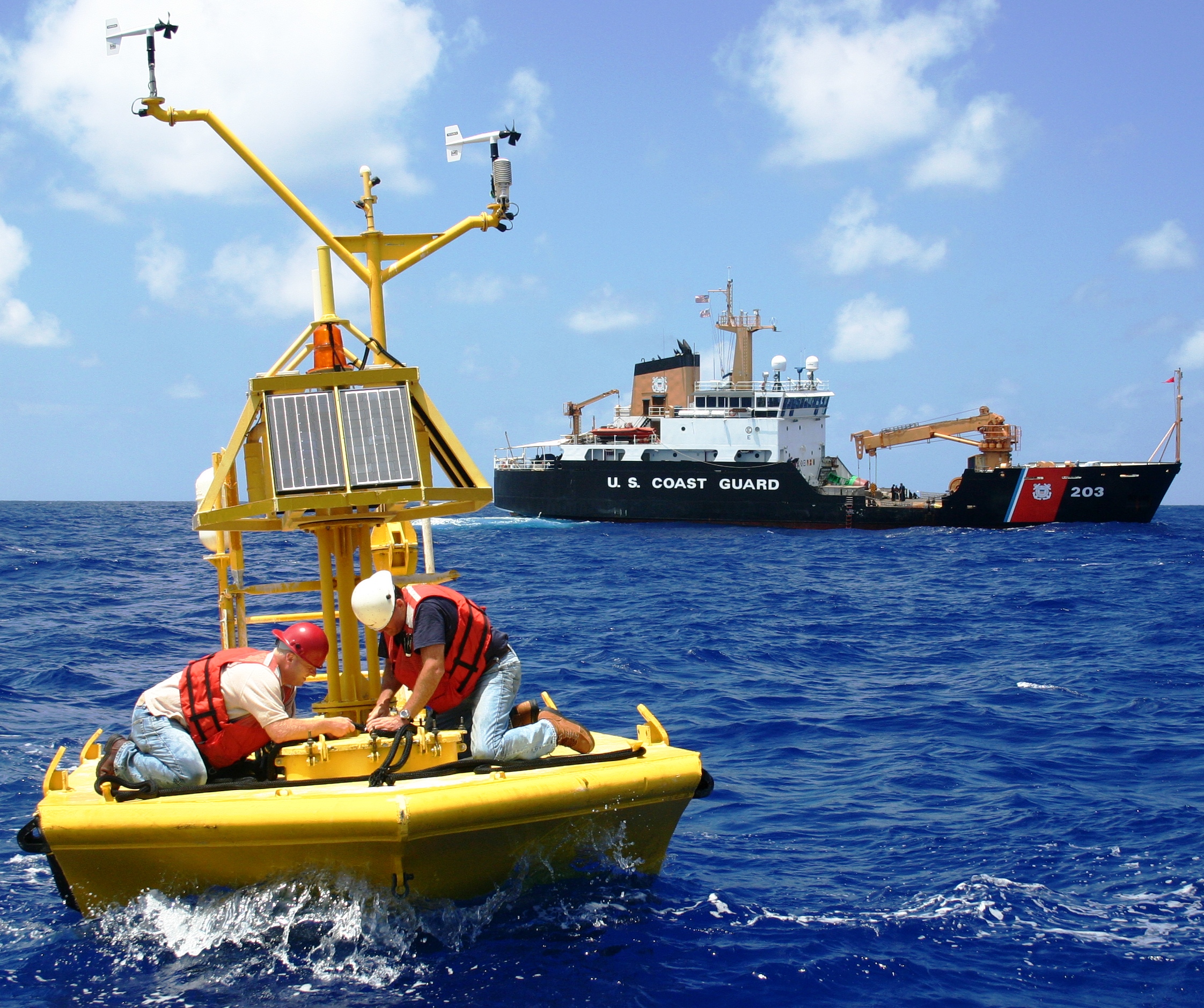 Workers performing maintenance of an ocean buoy at sea with a large ship in the background