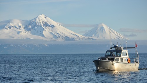 A NOAA boat at sea in front of snow covered mountains and clouds