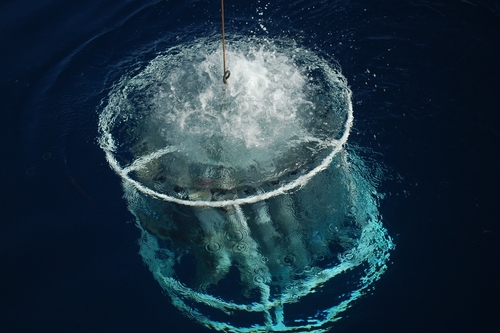 Conductivity, Temperature and Depth (CTD) sensor being lowered into the ocean with air bubbles at the ocean surface