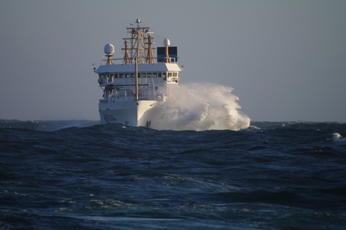 NOAA ship the Bell Shimada at sea with a large wave breaking on one side of the ship